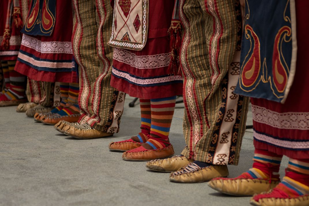 People wearing traditional, Armenian shoes with brightly colored pants and socks stand in a line. They are pictured from the waist down.