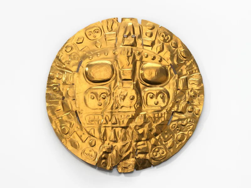 Against a white background, a shiny golden disc with raised features that depict two large, rounded eyes, the suggestion of a kind of face, and many interlocking diamonds, circles, lines and curved shapes