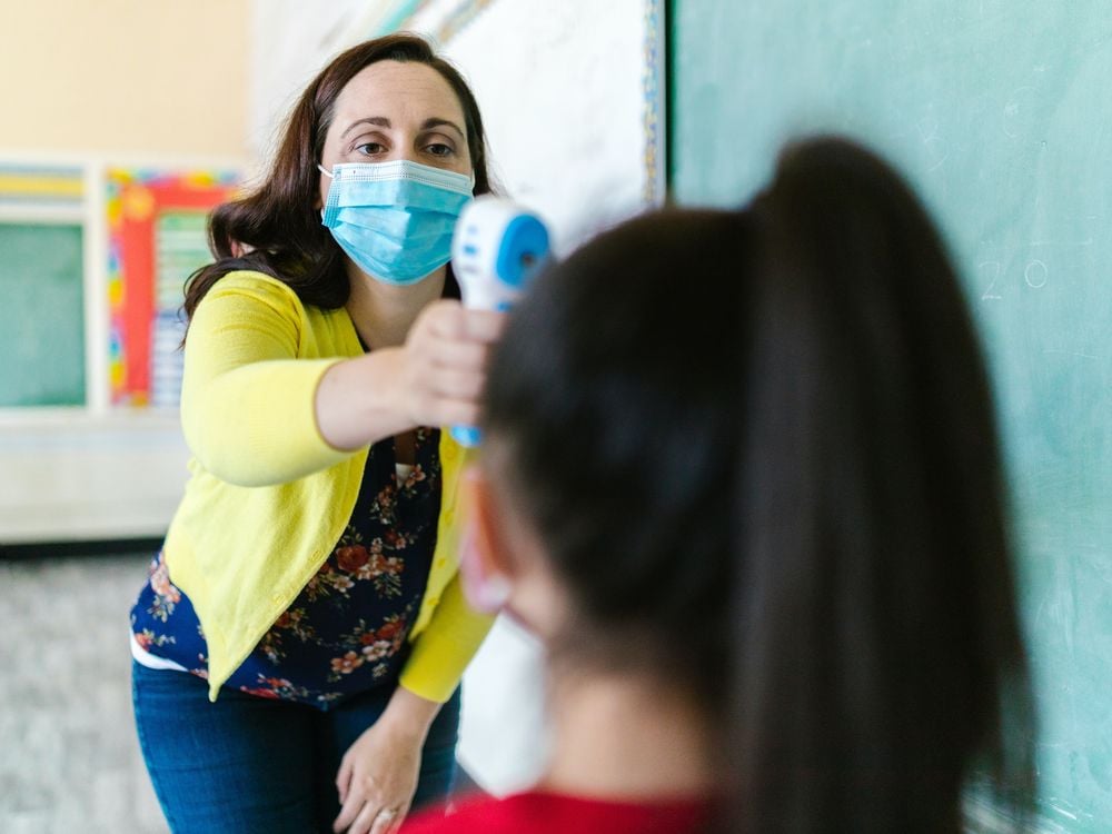 Woman wearing a mask taking a child's temperature
