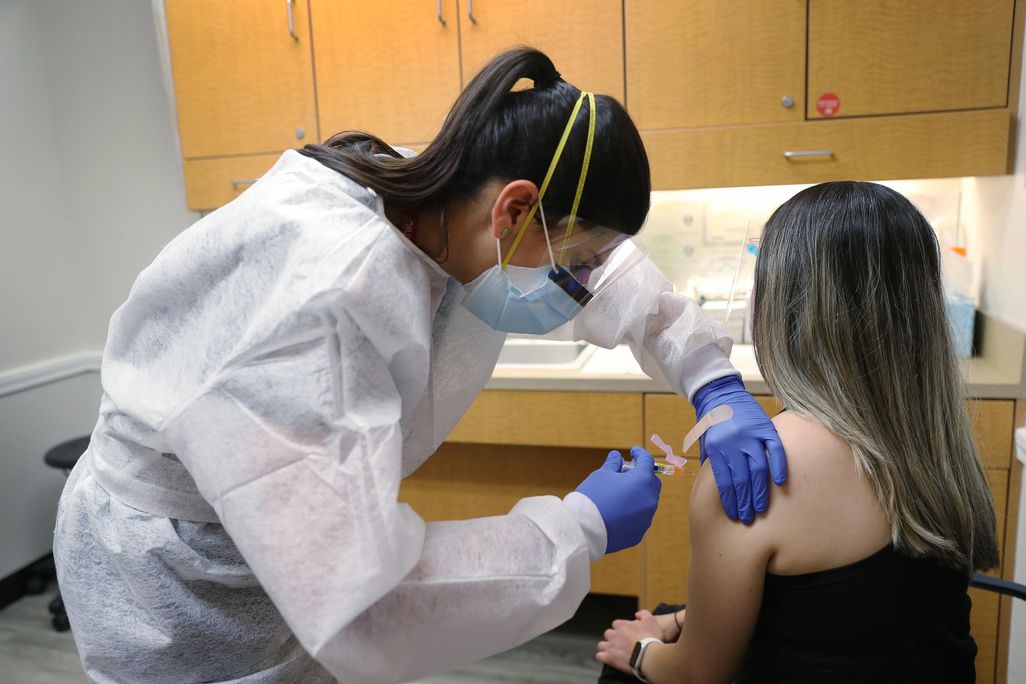 A nurse practitioner wears personal protection equipment as she administers a flu vaccination to a patient