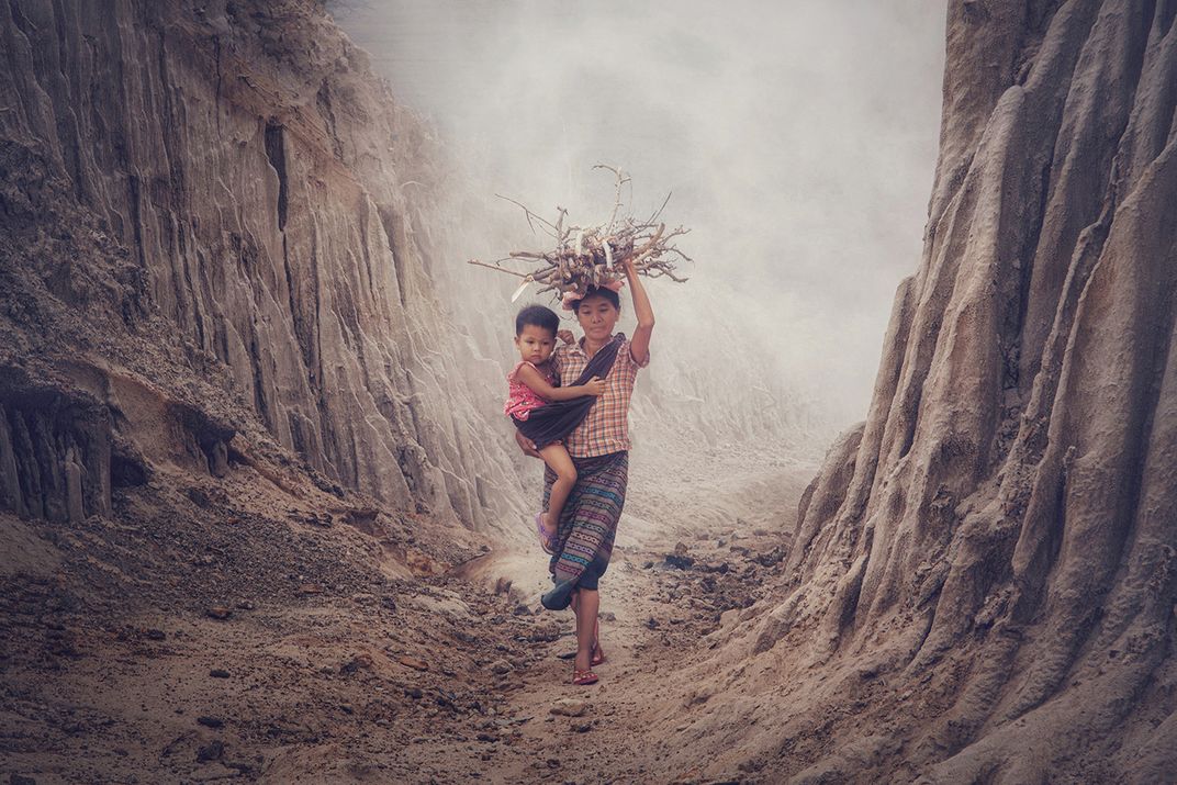 A toddler hitches a ride with mom as she carries firewood through a barren valley.
