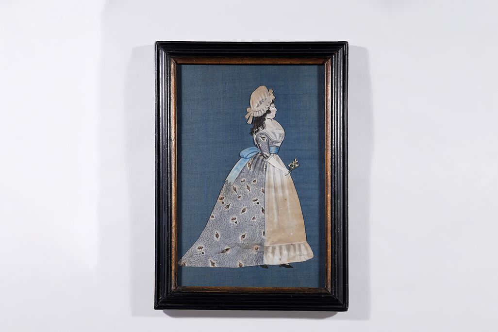 A vertical portrait of a woman in a full gown with a floral calico print on periwinkle; she holds a flower in one hand