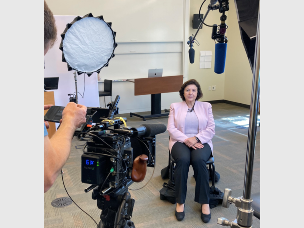 Annamarie Lusardi, seated in a chair facing a camera and lighting equipment.