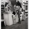 A woman and child stand at a shop counter facing a woman behind the register.