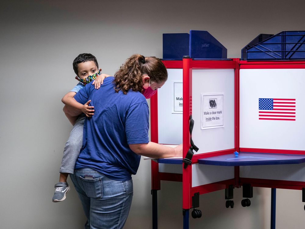 woman holding child and voting, both wearing masks