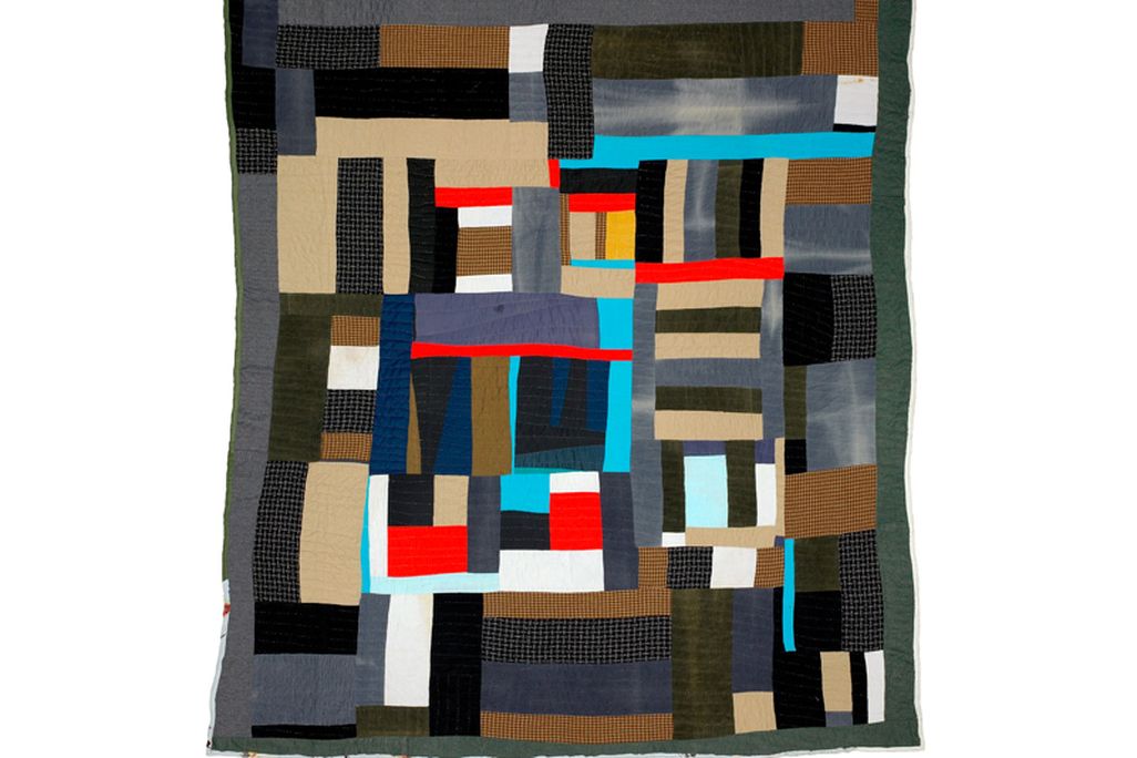 A quilt made of interlocking rectangles of dark green, gray, tan, with bright spots of light cyan, red and a tiny bit of yellow at the center