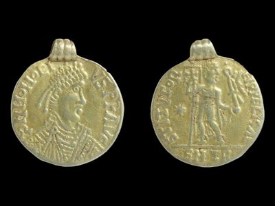 The coin features the bust of Honorius on one side. The other side depicts a person holding a&nbsp;banner or flag with a cross on it.