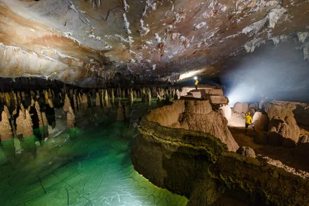 Cavers stand amongst large gour pool walls and unique raft cone formations inside Hang Va.