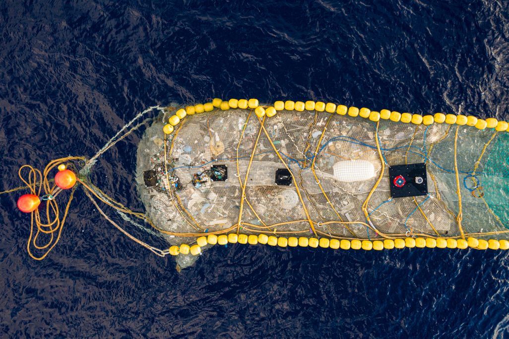 Ariel photo of trash collection device resembling floating pool lane lines with a large net filled with plastic trash