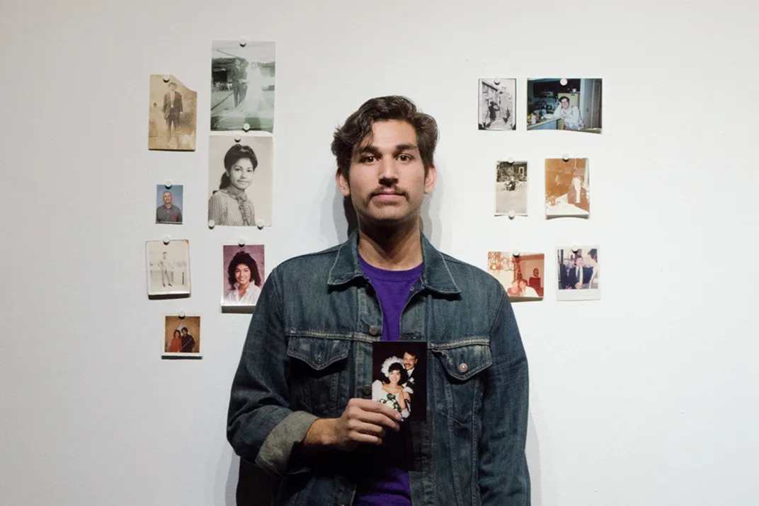 a man holds a photograph in hand with photograph behind him on a wall