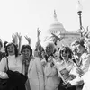 A group of smiling women pose for a picture with their hands up in a cheer in front of the U.S. Capitol.