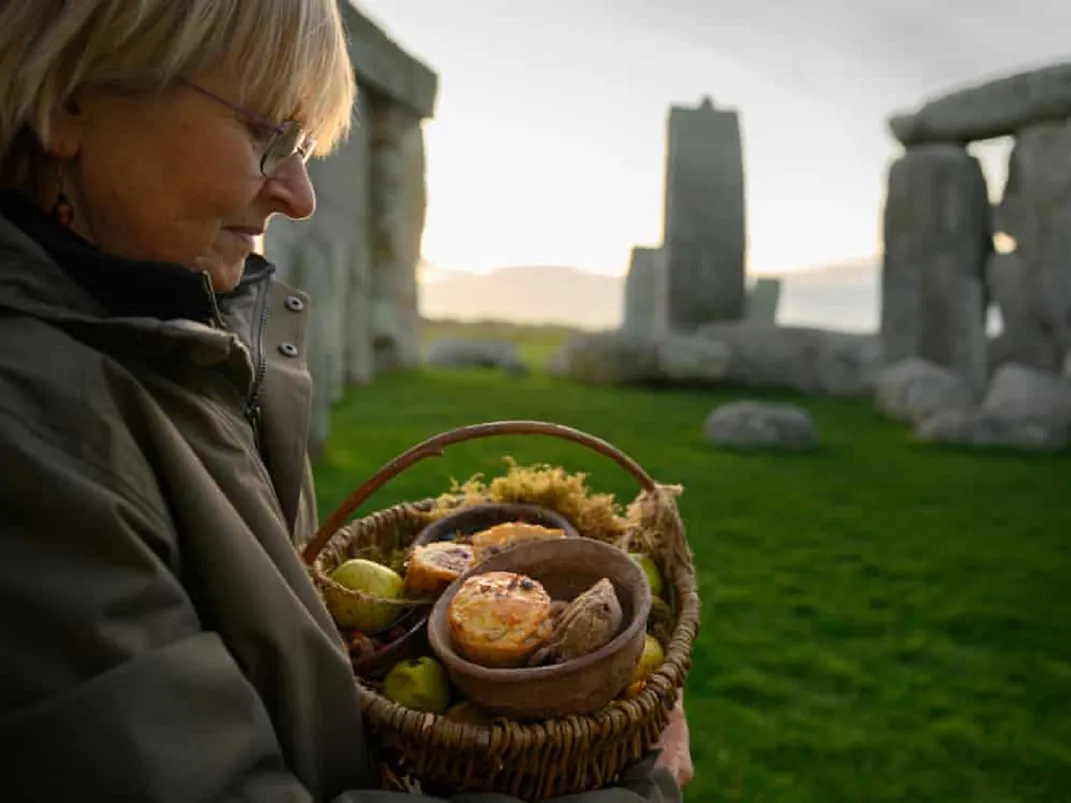 person carrying basket of pies in front of Stonehenge monument