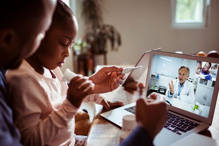 A father and his daughter engage in a video chat with their doctor.