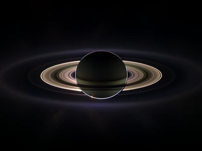 Saturn and its rings backlit by the sun, which is blocked by the planet in this view. Encircling the planet and inner rings is the much more extended E-ring.