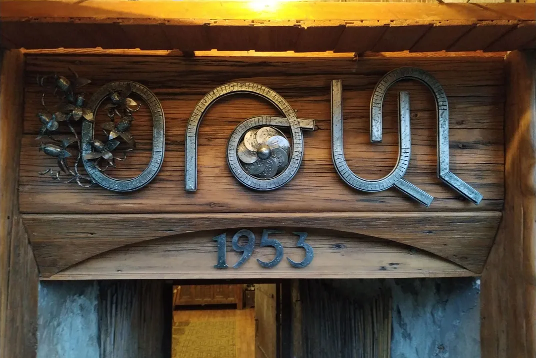 The top of a wooden entryway is heavily decorated with found-metal sculpture, greeting visitors.