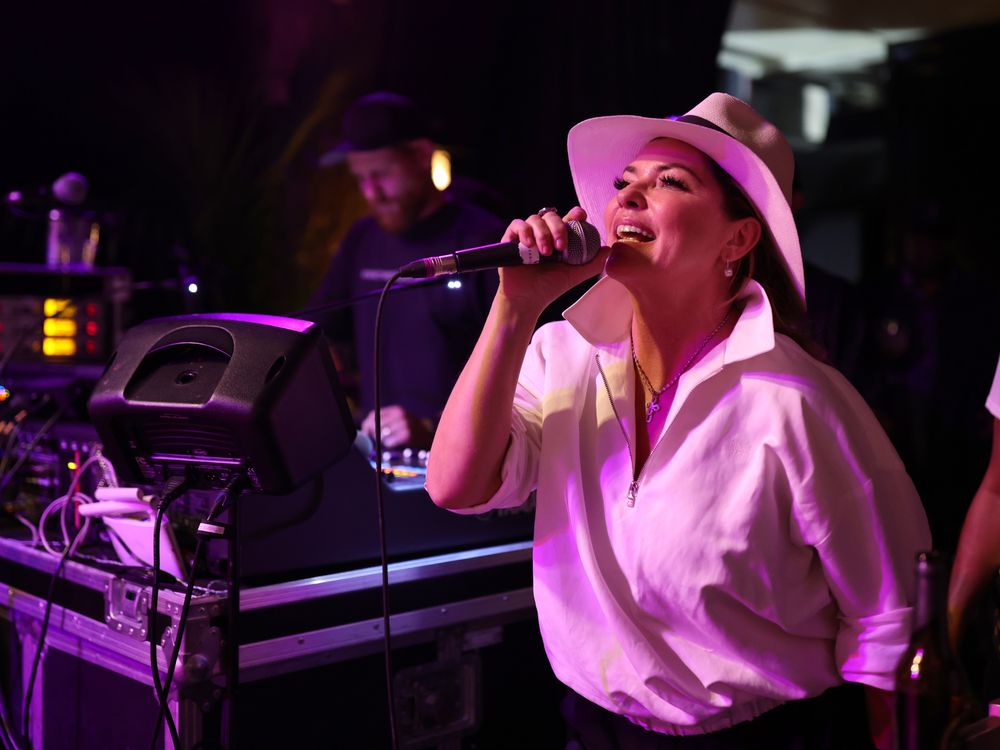 Shania Twain in a white shirt and hat singing on stage