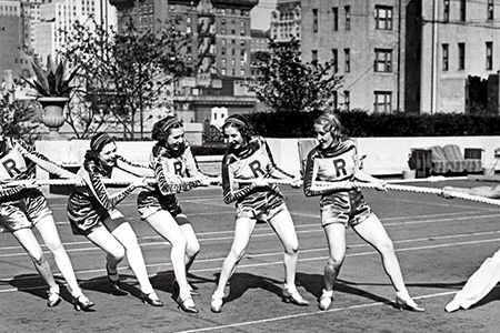 Charles Atlas playing tug of war with the Rockettes atop Radio City Music Hall