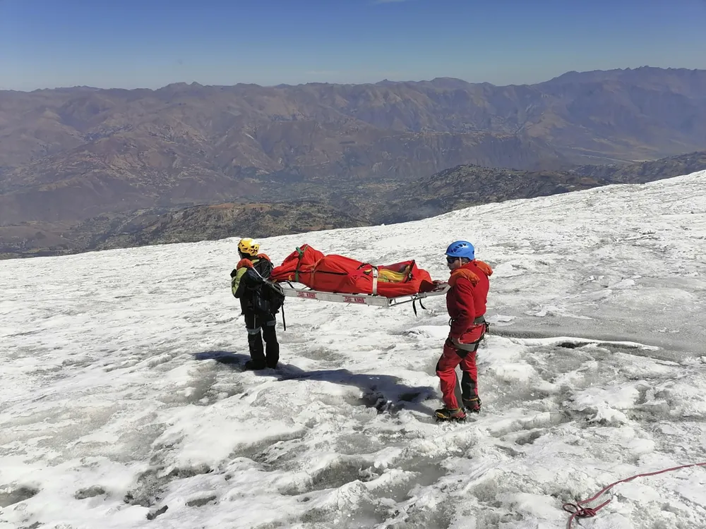 Two rescuers carrying a stretcher down a snowy mountain slope