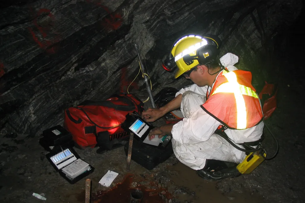 man crouched next to materials and a rock wall