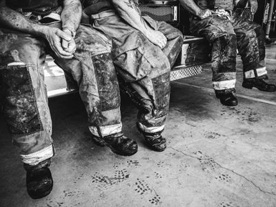 Firefighters, still dressed in their smoke- and soot-stained bunker gear, take a breather after a harrowing day of battling a particularly stubborn brush fire.