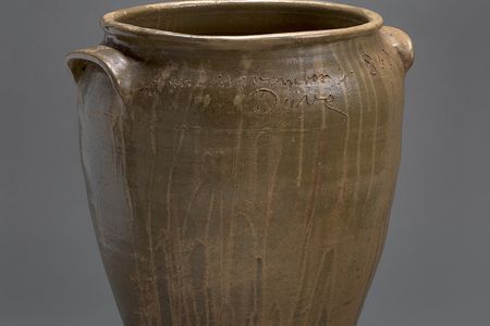 A brown, ceramic vessel with an inscription and the artist's name "Dave" carved around the opening.