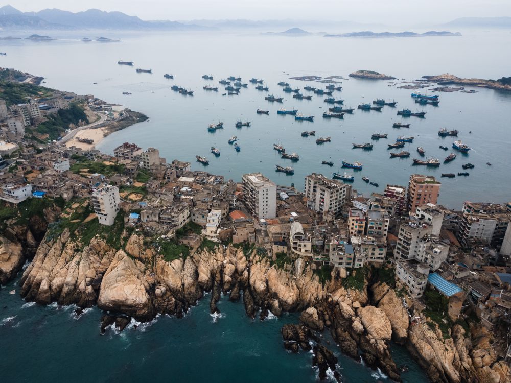 A cliff-top fishing village clings to a narrow headland: surf hammers the south face while a fleet shelters in the north cove, idle until the season opens.