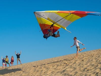 The call of the sky is strong in Kitty Hawk. Not far from where the Wright brothers first flew, student Hannah Zobel glides over sand dunes after a lesson with Luke Robinson (running) of Kitty Hawk Kites hang gliding school.