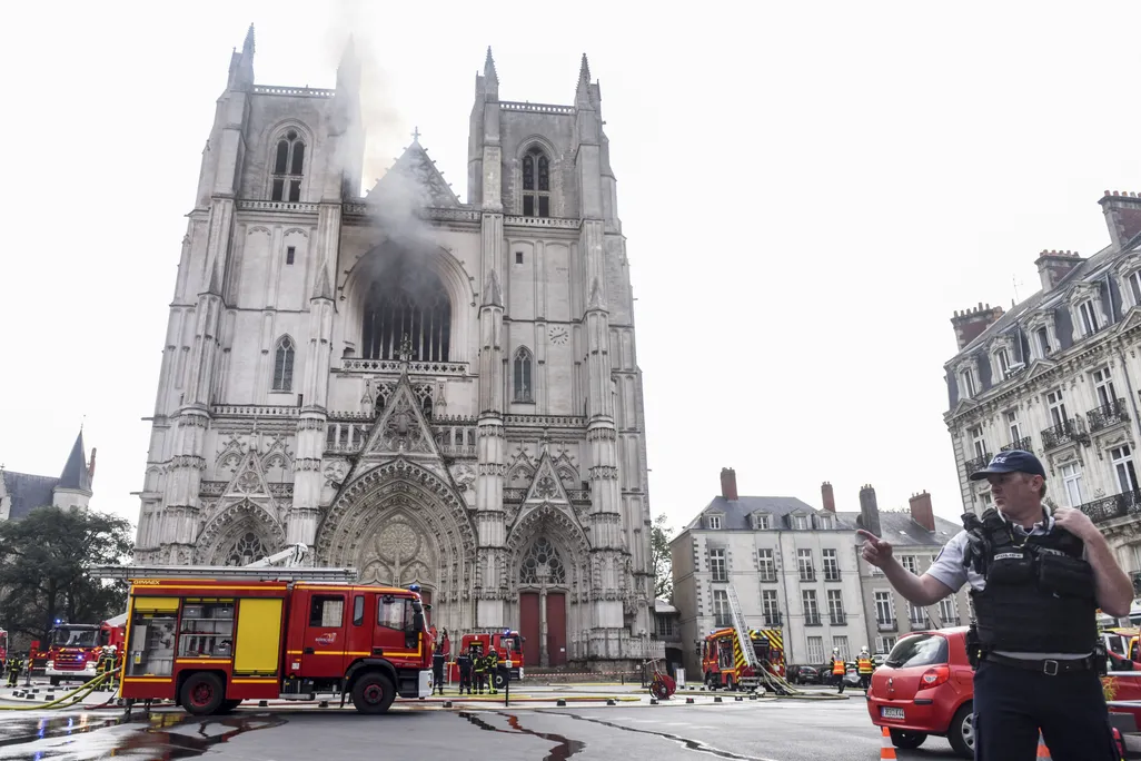 Cathedral in Nantes with black smoke, a firefighter's truck in the foreground