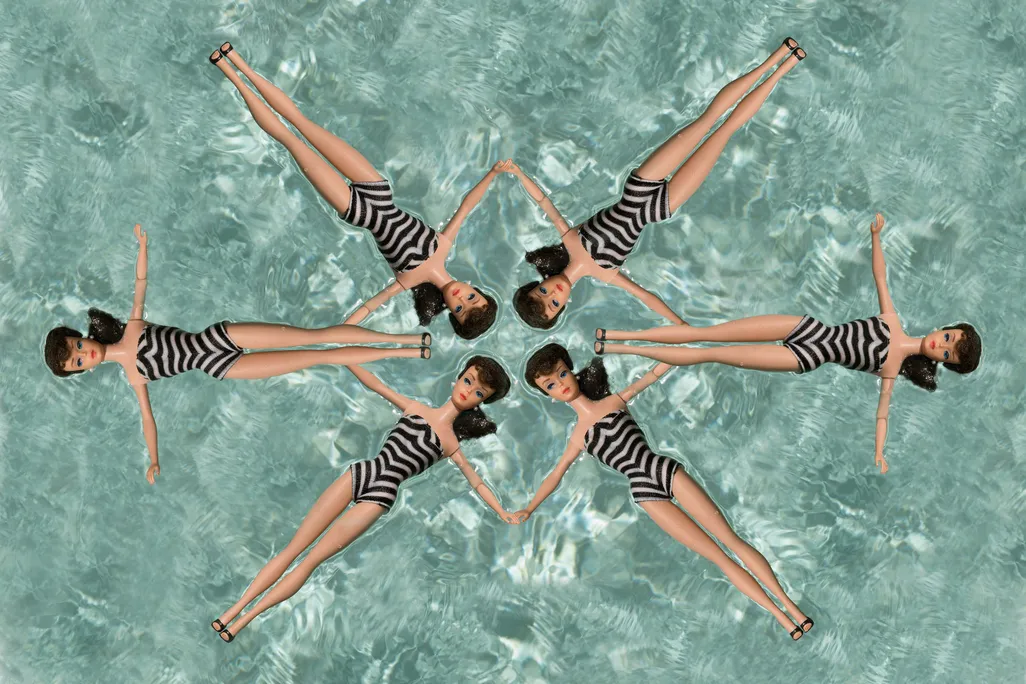 six Barbie dolls wearing zebra striped swimsuits in a synchronized formation in a swimming pool