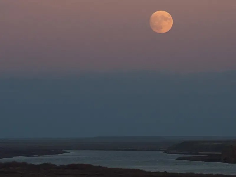 a full moon appears orange in the sky above a river