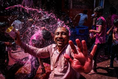 A reveler enjoys a playful and colorful water war in the streets of Jodhpur during the Holi festival.

