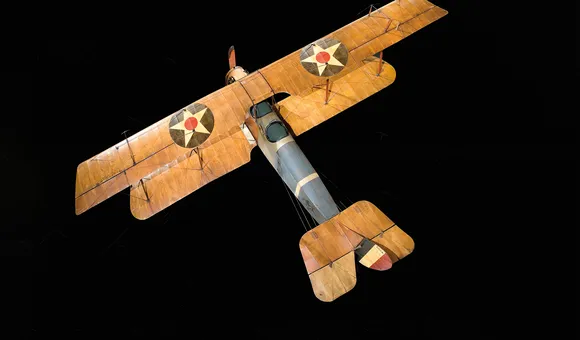 A wood and fabric World War I-era Curtis JN-4D aircraft is on display at the National Air and Space Museum. It has tan wings, and a brown and blue fuselage.