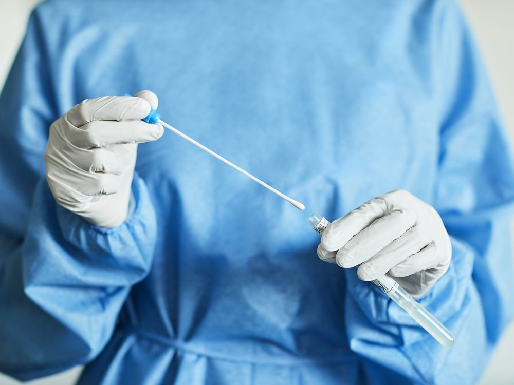 A female doctor in a blue surgical gown holding a long cotton swab used for covid-19 testing