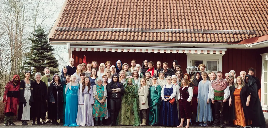 Dozens of adults in fantasy costumes pose outside a red-tile-roofed building.