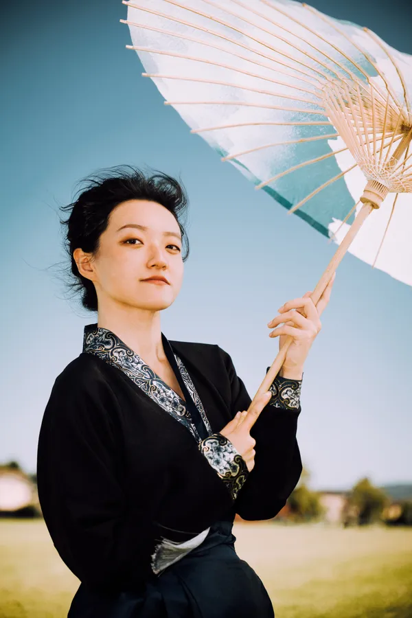 Ethereal Grace: A Woman with Bamboo Umbrella in Traditional Attire Against Azure Skies thumbnail