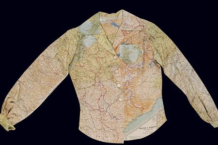 A ladies long-sleeve blouse fastened by four plastic white buttons hangs against a dark background. The blouse features a multi-color map pattern printed on a white silk background.