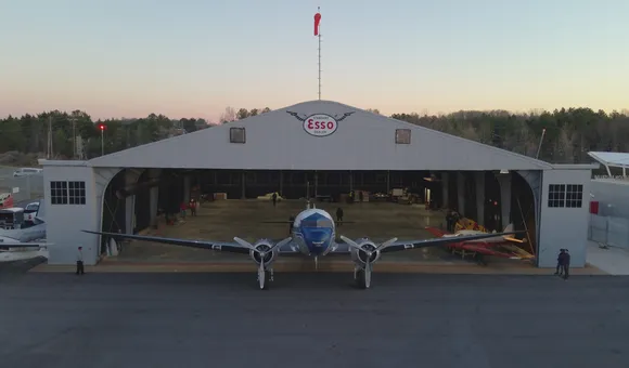 A propellor plane is in front of an open hangar