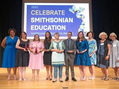 A group of people posing for a photo on a stage.  Dr. Monique M. Chism with Awardees and Smithsonian Women’s Committee supporters at the 2022 Smithsonian Education Awards Ceremony, July 28, 2022.