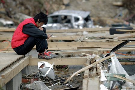A man holds his mobile phone as he sits in the ruins of a house in Minamisanriku, Japan, after the area was devastated by a magnitude 9.0 earthquake and tsunami in March 2011.