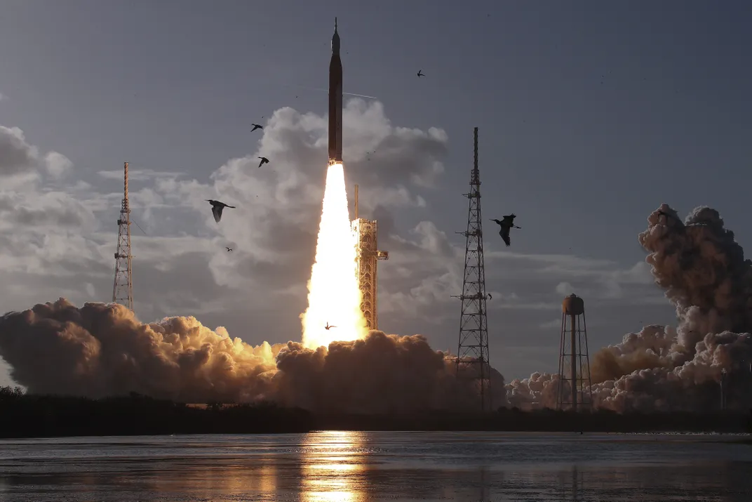 silhouettes of birds fly past a launching rocket