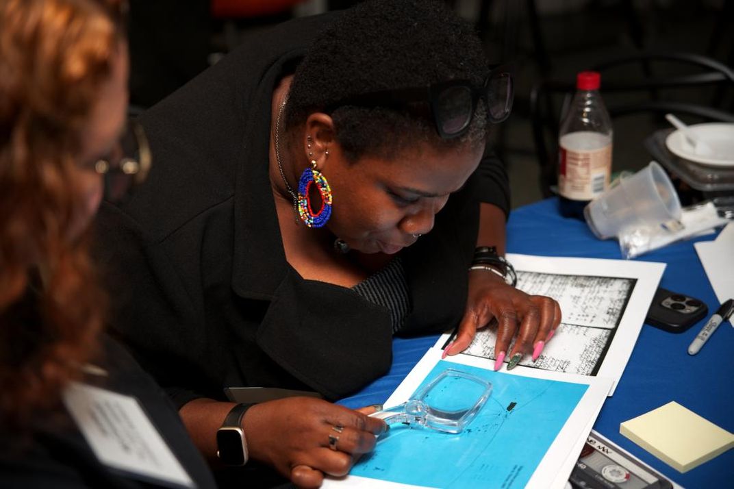 A woman looks closely at a document in front of her using a magnifying glass.