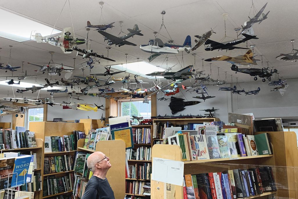 man looking up at model planes above bookshop shelves