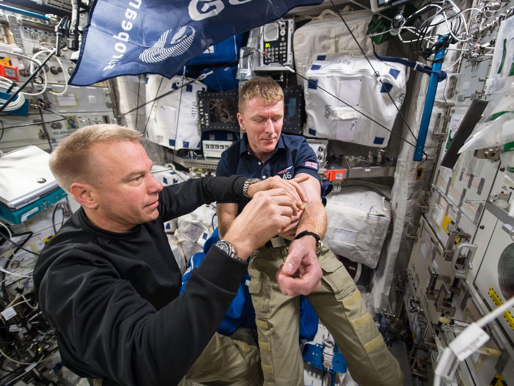 A male NASA astronaut Tim Kopra performs blood draw on European Space Agency astronaut Tim Peake on the international space station
