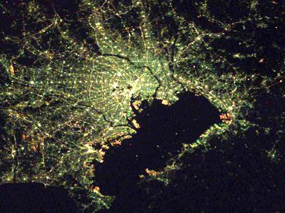 Tokyo, typified by the blue-green lighting of Japan's cities, curves around its bay. The Emperor's Palace is visible as the dark spot in the city center, as is Narita International airport, a bright point of light to the east.