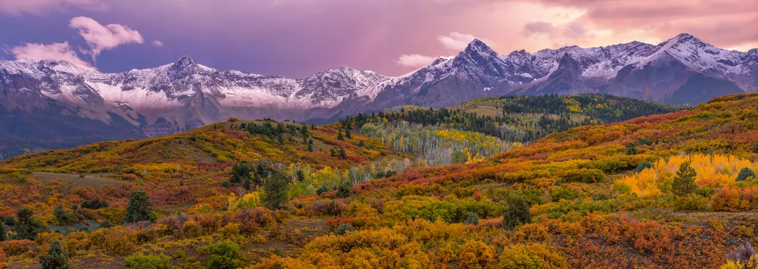 9 - Beautiful trees blanket the landscape near a snowcapped mountain range.