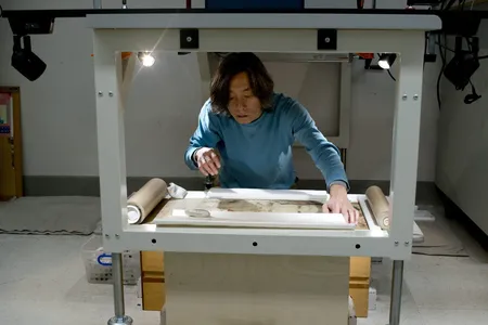 Conservator Jiro Ueda positions the handscroll prior to reflectance imaging spectroscopy. A large camera mounted above his head captures images through a hole in the table