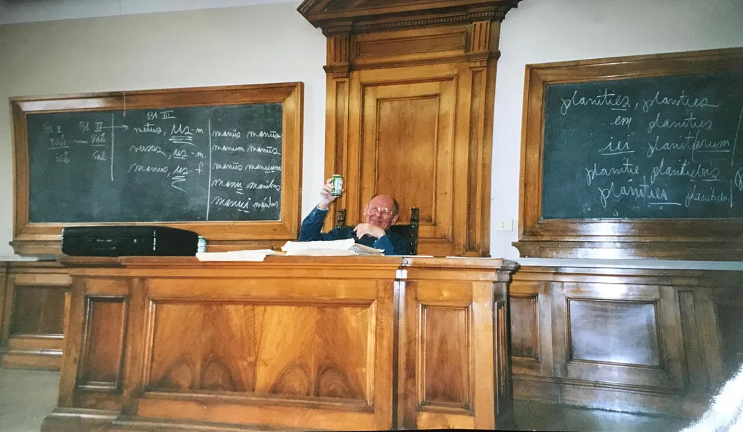 Photo of Father Foster sitting at desk in front of chalkboards