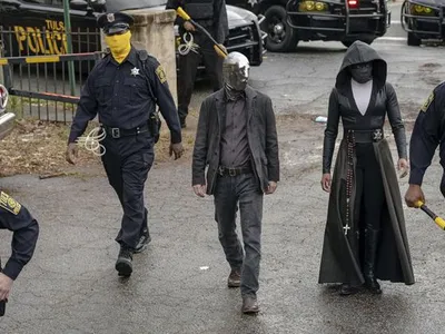 In a scene from the HBO series, Tulsa’s masked police force prepares for a raid. Detective Wade Tillman (known as “Looking Glass”) is played by Tim Blake Nelson. Detective Angela Abar (known as “Sister Night”) is played by Regina King
