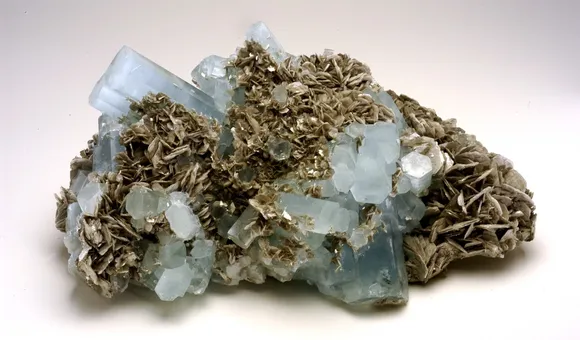 A chuck of natural, light blue and gray aquamarine beryl on white background.