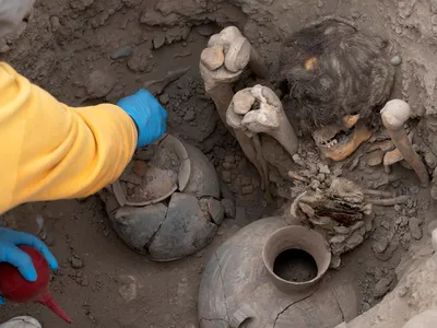 A worker uncovers the mummy, which belonged to the Ychsma culture, buried in a shallow funeral chamber during an excavation in the Huaca Pucllana on September 5, 2023.